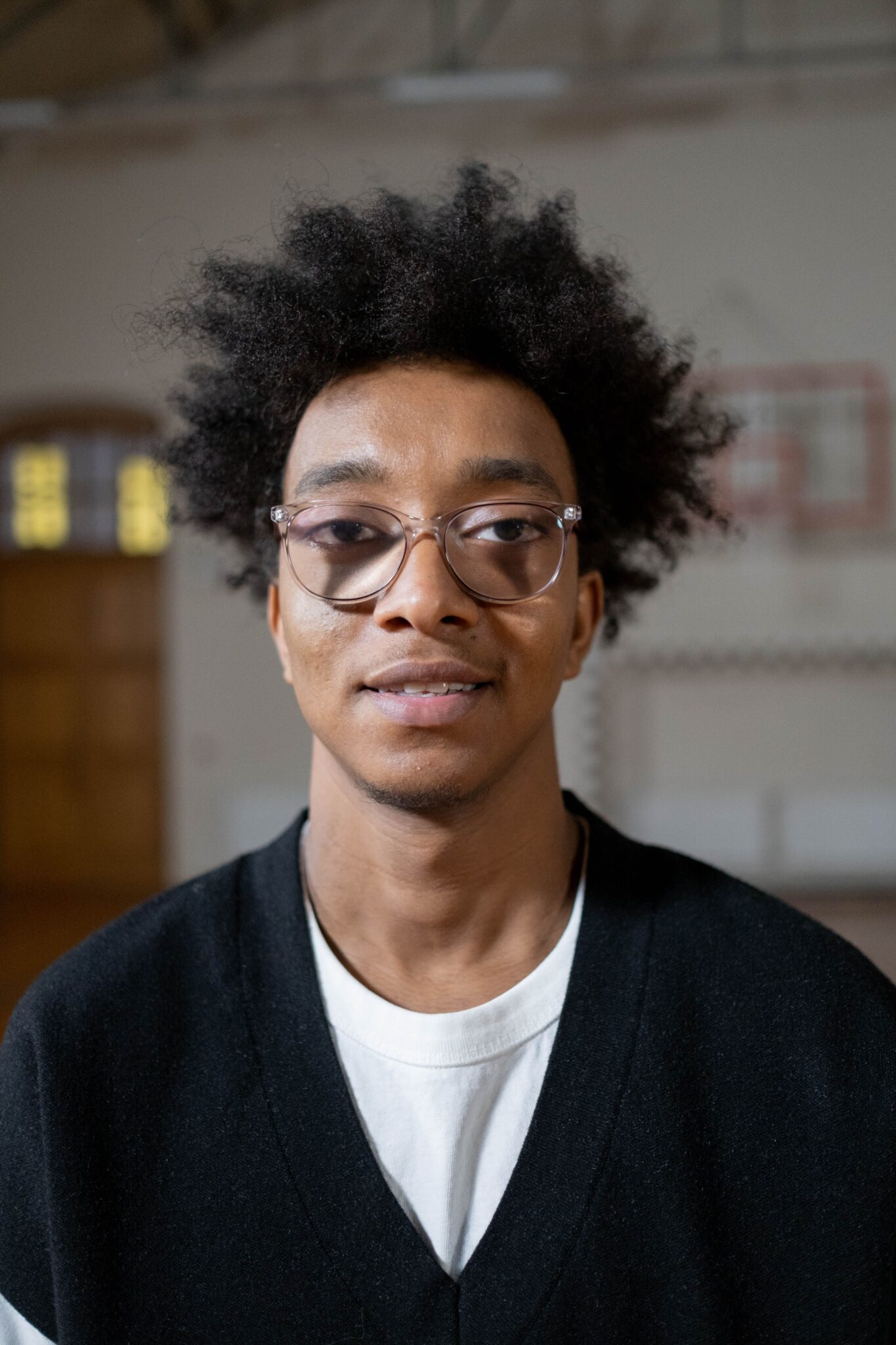 Young man with glasses and afro hair smiling indoors. Casual portrait capturing a relaxed vibe.